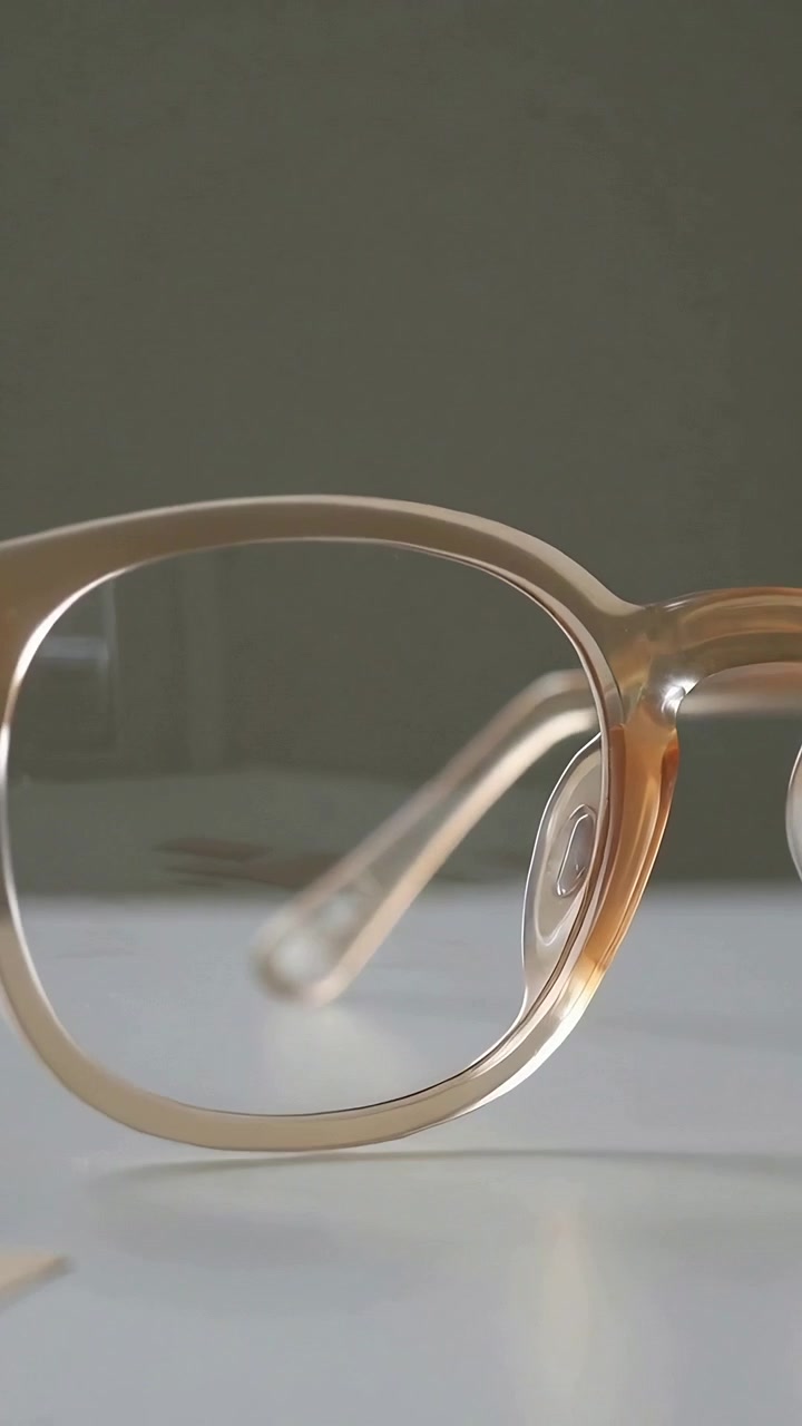 Vertical video: Shifting camera revealing amber acetate glasses resting on desk showing nose pads