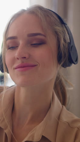 young blonde haired woman with ponytail in headphones enjoys music moving to beat against bright window in comfortable home room slow motion closeup