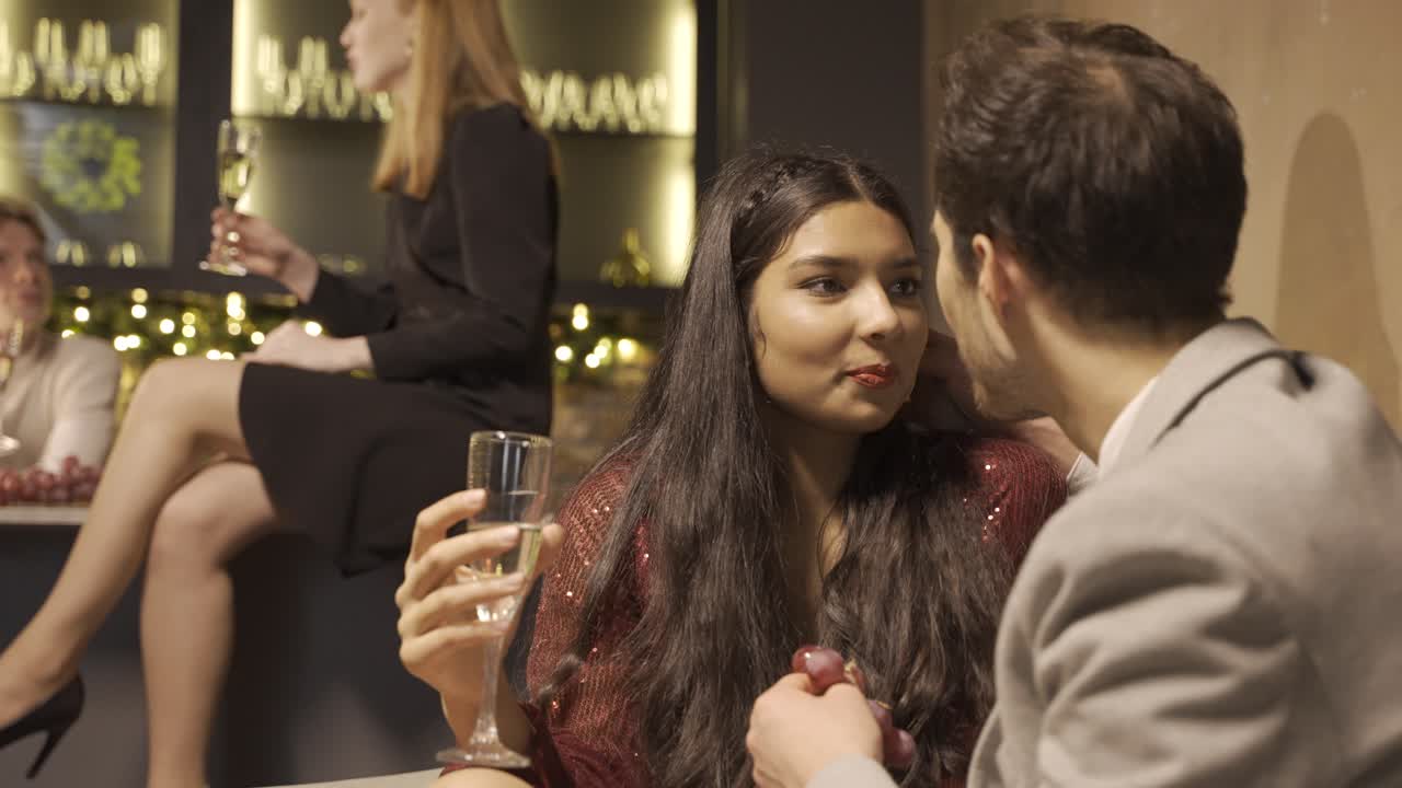 Close-up view of a couple celebrating the New Year's party with friends, they are sitting at a table while eating grapes and drinking champagne with great complicity