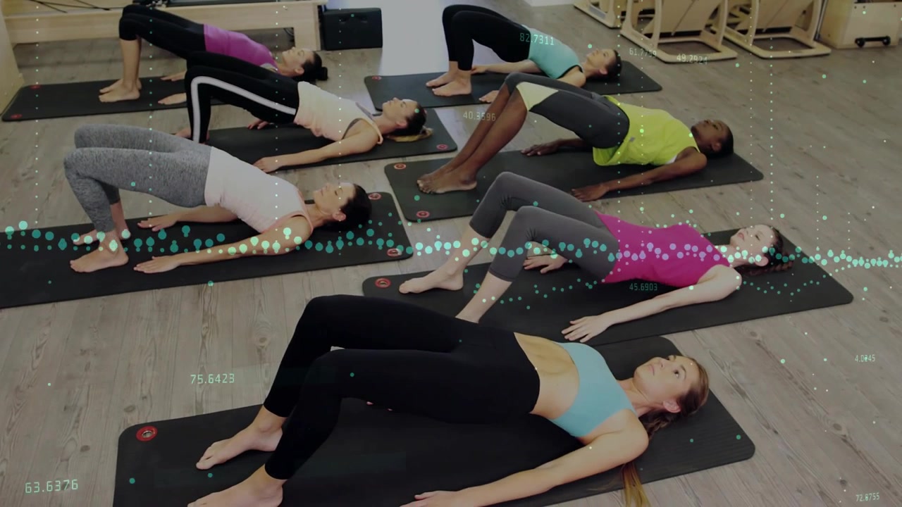 Kobieta na pierwszym planie wykonująca mostek, unosząca biodra w rytm fali fitness synchronizującej się z ćwiczeniami na matach