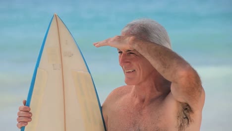 Closeup-of-a-senior-man-looking-at-the-ocean-with-a-surfboard