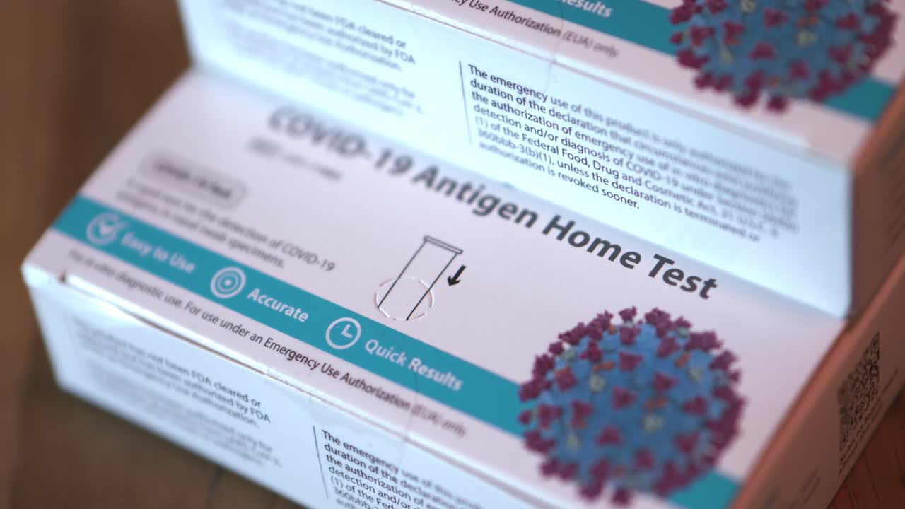 Covid 19 at home Antigen test kit for coronavirus 3 white and blue boxes of tests stacked up close panning shot focusing on bottom box and slowly pulling out with close focus.