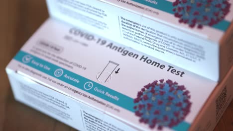 covid 19 at home antigen test kit for coronavirus 3 white and blue boxes of tests stacked up close panning shot focusing on bottom box and slowly pulling out with close focus.