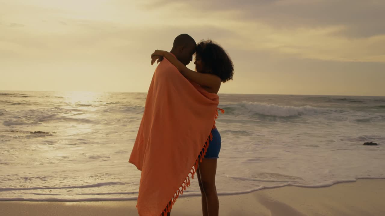 vista lateral de una pareja afroamericana envuelta en una manta en la playa 4k