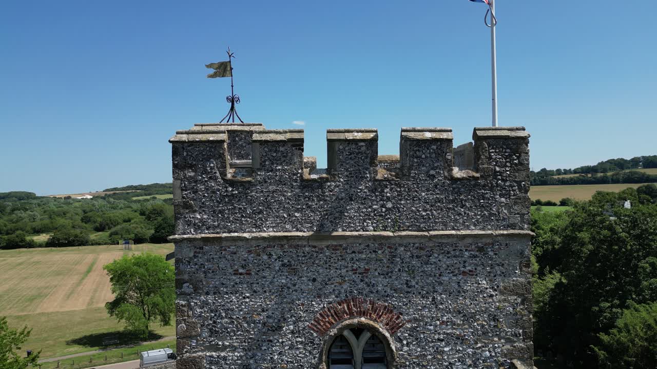 A rising boom-shot of the tower of St Mary's church in Chartham, rising to show the union flag flying in front of stretching fields