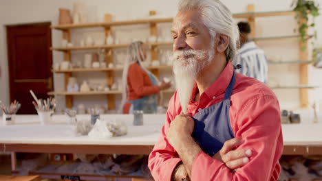 Feliz-Alfarero-Birracial-Con-Barba-Larga-Sentado-Y-Sonriendo-En-Un-Estudio-De-Cerámica,-Cámara-Lenta