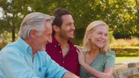 smiling family with mature parents and adult son on walk in summer countryside