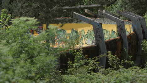 rack focus from green brush to curved segment of the bobsleigh and luge track in sarajevo, bosnia. old graffiti ruins from the winter olympics.
