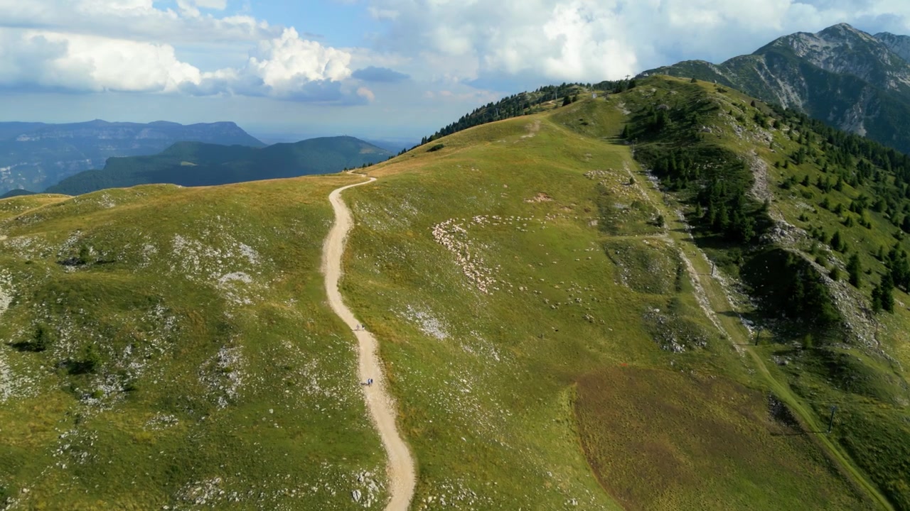 Veduta aerea di escursionisti su un sentiero di montagna tortuoso con cime e un lago distante sottostante