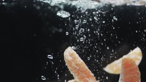 Video-of-slices-of-orange-falling-into-water-with-copy-space-on-black-background