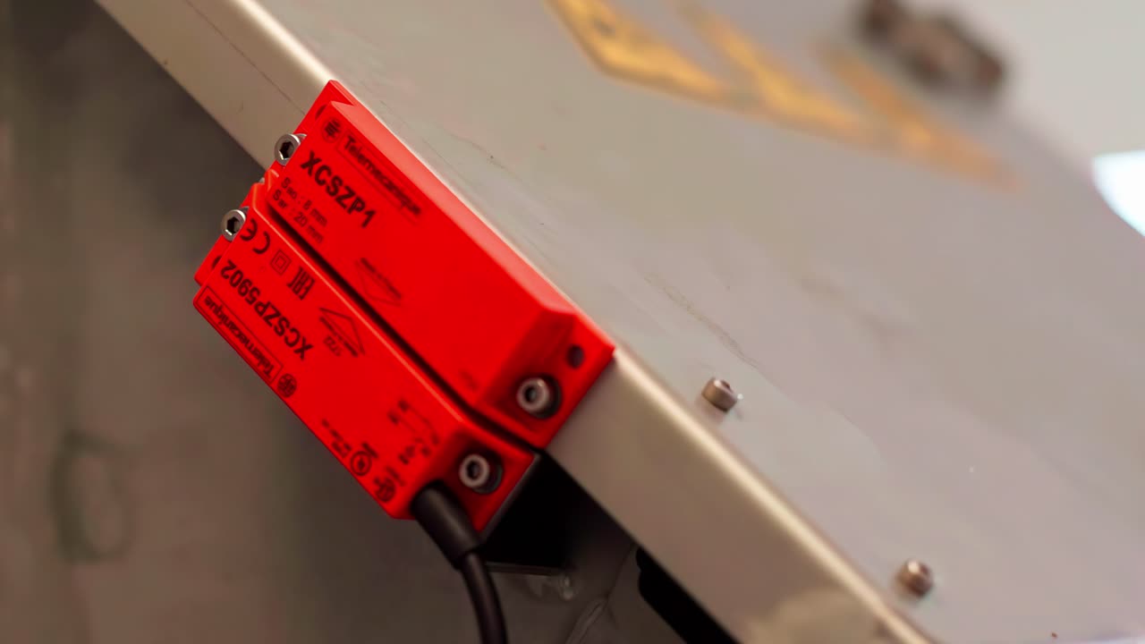 Red safety interlock switch on metal machinery in factory setting