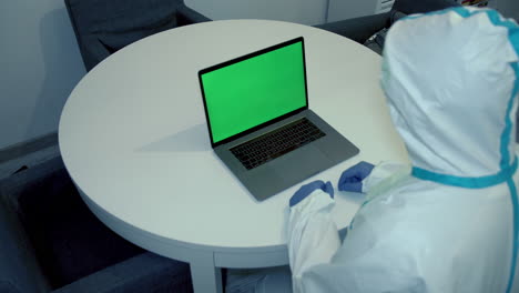 medical professional in ppe suit, protective gloves and mask in covid-19 hospital evaluating diagnosis on laptop