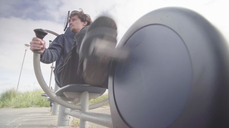 A young male wearing dark clothing exercising on an exercise bike outdoors
