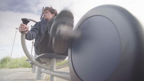 a young male wearing dark clothing exercising on an exercise bike outdoors