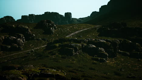 a winding path leads up a grassy mountainside with rocky cliffs and a clear blue sky