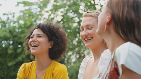 three female friends sitting outdoors in summer garden at home relaxing and talking