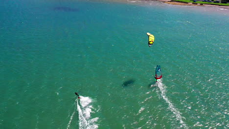 Kiteboarder-and-windsurfer-surf-near-Joaquina-Beach,-Brasil,-aerial-shot