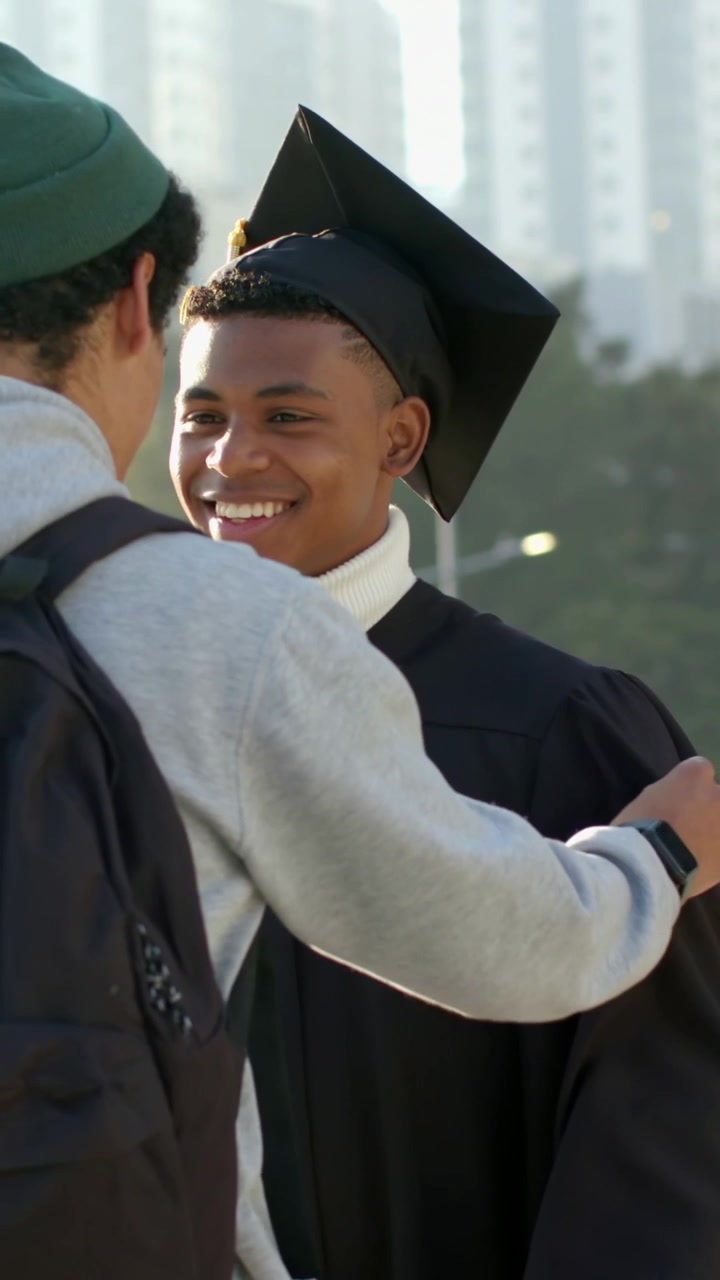 Vertical video: Coming friend patting grad in gown, smiling, holding diploma, celebrating outdoors