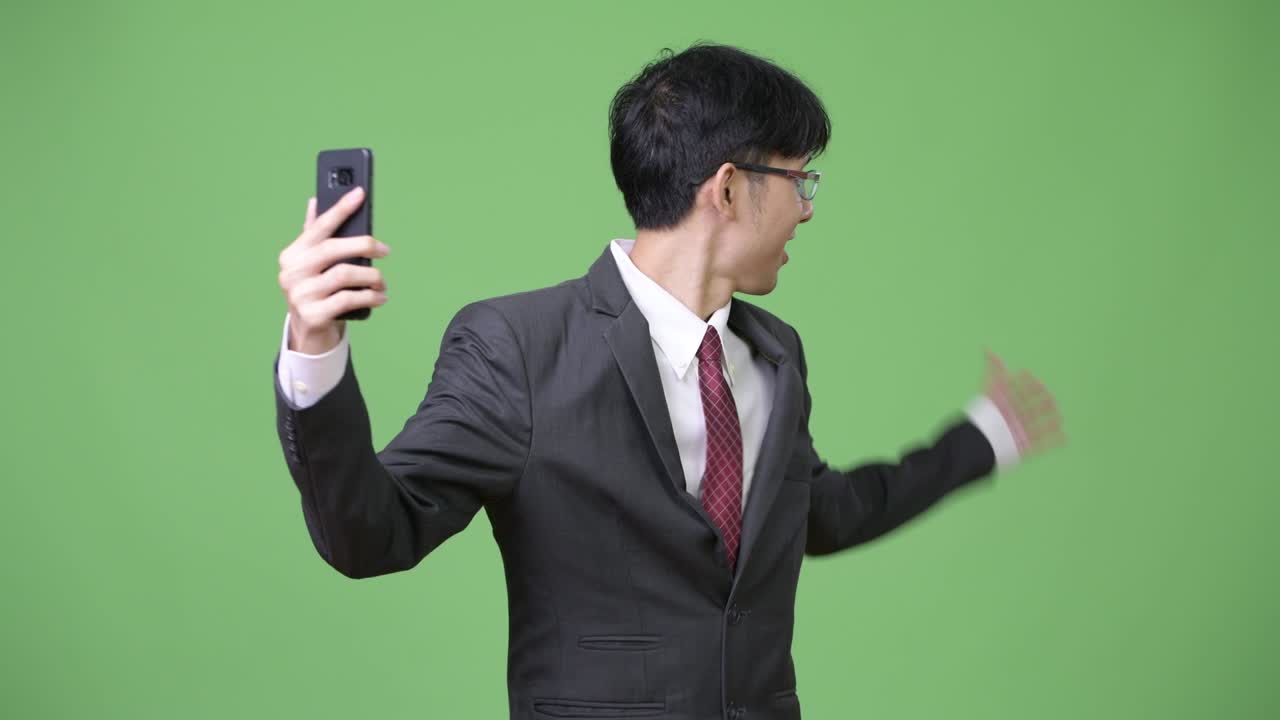 젊은 행복 한 아시아 사업가 가 전화 로 비디오 통화 하는 동안 미소 짓고 있다