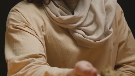 studio shot of man wearing robes with long hair and beard representing figure of jesus christ breaking and offering bread