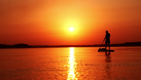 bright setting sun reflecting in the river. black male silhouette sup boarding on the river at sunset.