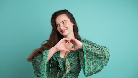 happy woman blowing kiss and showing heart gesture in blue studio