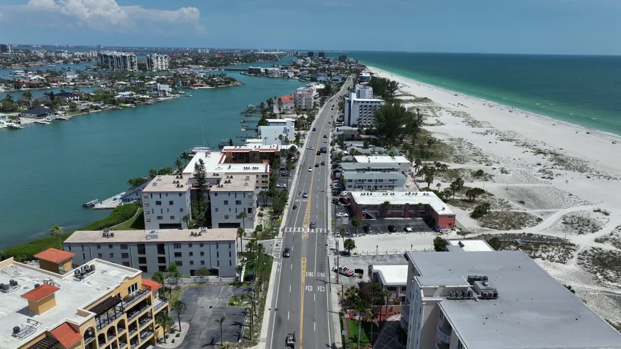 Treasure island with sandy beach and sea on one side and river channel and luxury houses on other side. Sunny day in Florida. Traffic scene. Aerial rising wide shot