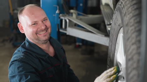 mecánico en uniforme azul sonriendo mientras frota la mano con un guante blanco en el borde del coche, mostrando cuidado meticuloso y atención en el taller de reparación de automóviles