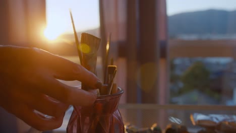 artist working in a studio with paintbrushes and sunset view.
