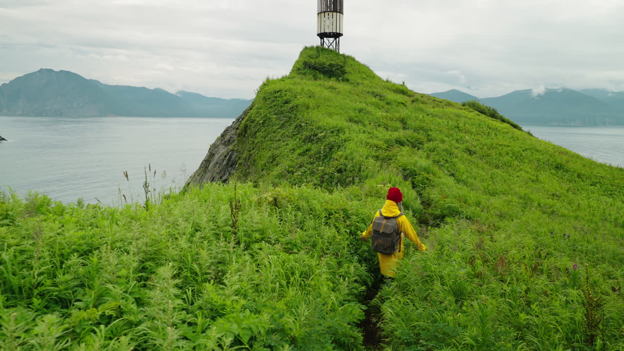 Hiking on a grassy hill overlooking the ocean, with a lighthouse in the background.
