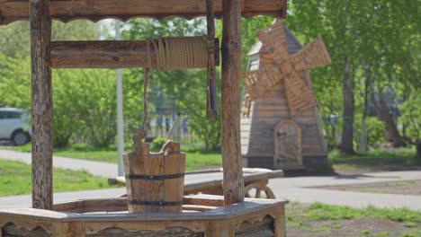 a wooden well with a bucket and a windmill in the background in the park.