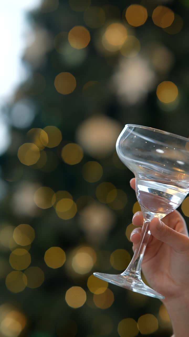 mano sosteniendo un vaso de cóctel frente a un árbol de navidad