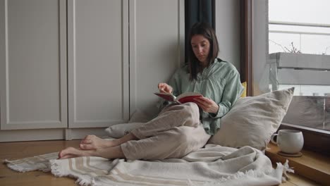 mujer leyendo un libro junto a la ventana