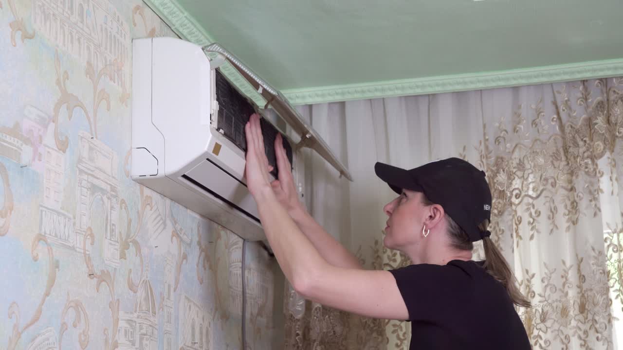 Woman inspects condition of household air conditioner. She opens its lid and is surprised by state of filters.