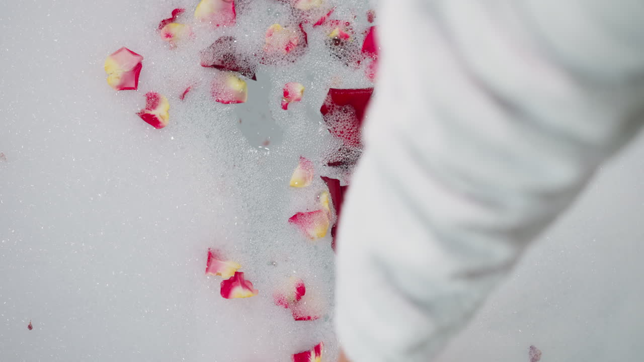 여성은 욕조에서 꽃잎으로 거품을 니다. 여자는 호텔 방에서 신선한 꽃으로 만적 인 목욕을 준비합니다. 스파 살롱에서 보디 케어 의식