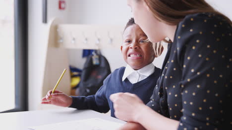 Joven-Maestra-De-Escuela-Primaria-Trabajando-Uno-A-Uno-Con-Un-Colegial-En-Un-Salón-De-Clases,-De-Cerca