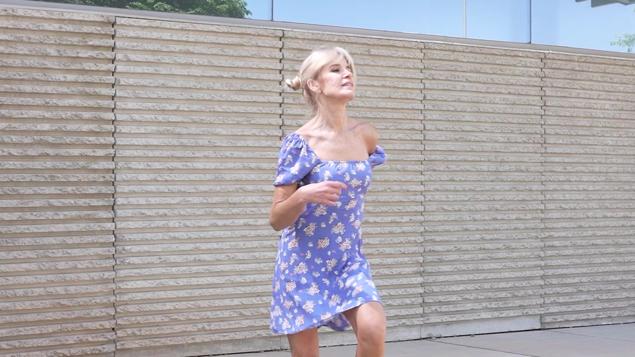 Una bellissima donna bionda con un elegante vestito floreale passeggia per una città alla moda in una giornata di sole.