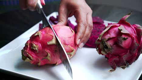 Hermoso-Primer-Plano-De-Cuchillo-Cortando-Fruta-De-Dragón-Rojo-En-Un-Plato-Blanco-Fruta-De-Dragón-Roja-Y-Blanca-Rebanadas-De-Fruta-De-Dragón-Rojo-Y-Cultivando-Plantas-Exóticas-Pitaya