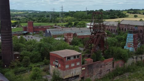 abandoned old overgrown rusting coal mine industrial wheel buildings aerial view dolly right