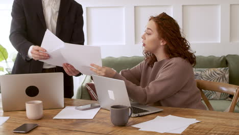 woman sitting at table with laptop computer giving blank papers to her male colleague