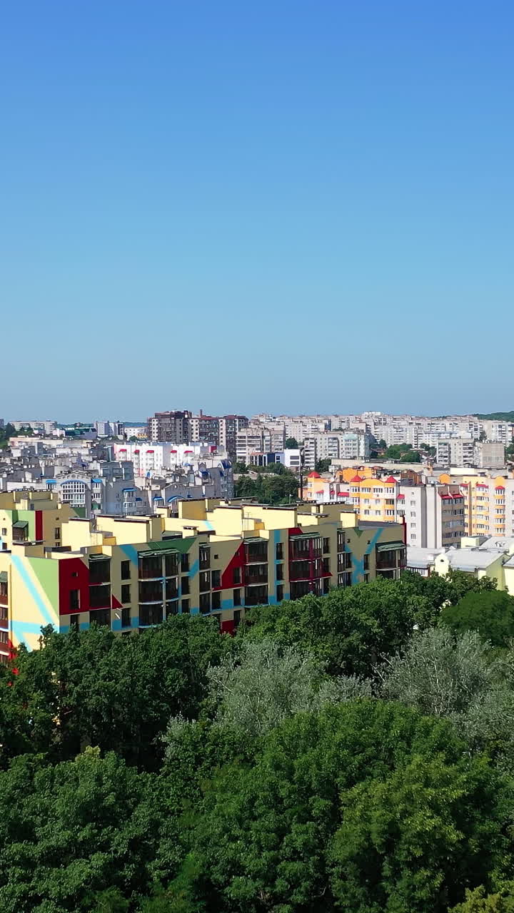 Colorful residential complex in the city. Flight over green trees on the urban background. Contemporary part of a city. Aerial view. Vertical video