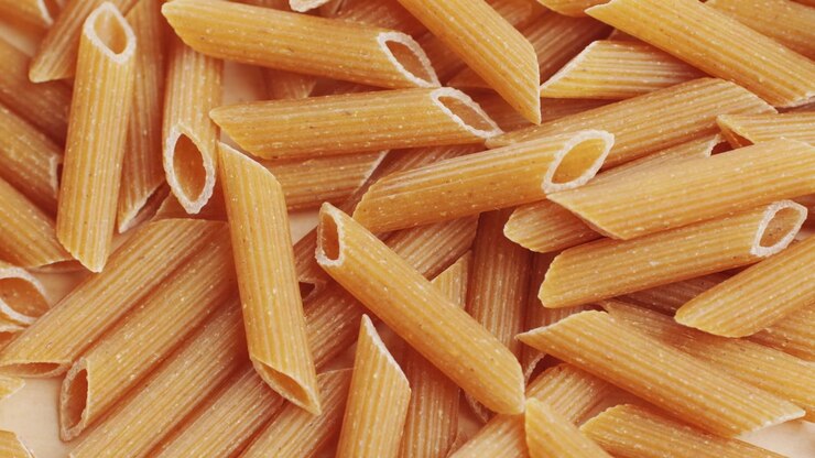 Pasta integrale biologica, maccheroni di semola di grano duro, penne rigate crude in una ciotola di legno. Filmato 4k di alta qualità