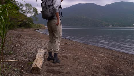 male hiker taking break sitting on leg next to beautiful lake on clear day