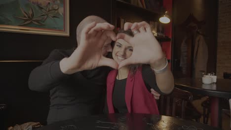 Couple in love making heart shape with hands in a cafe