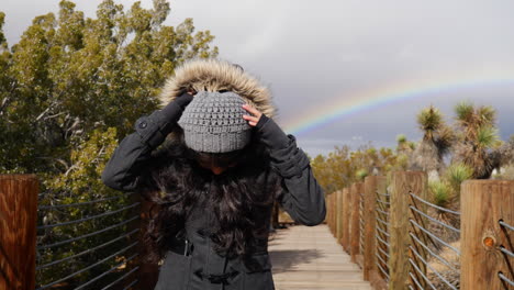 a happy, pretty woman smiling to rejoice after a rain storm with a colorful rainbow in the cloudy dark sky after bad weather slow motion