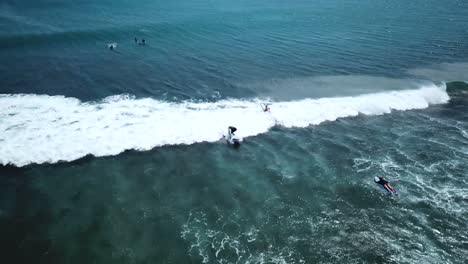 Drone-Shot-following-two-surfers-at-Padang-Padang-Beach-in-Bali,-Indonesia
