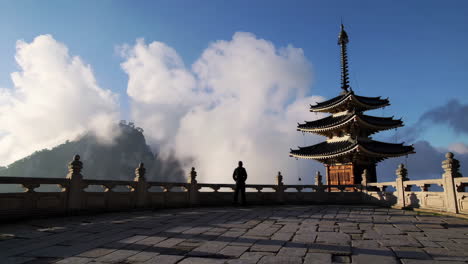 person admiring a traditional pagoda and misty mountain landscape