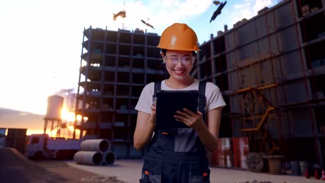 trabajadora asiática con gafas de protección y casco de seguridad usando una tableta mientras está de pie en el sitio de construcción