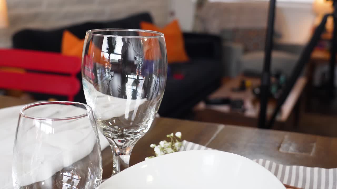 Romantic Dining Table Set for Dinner with White Plates and Wine Glasses next to Living Room Couch, Gimbal Movement, Gold Silverwhere, Forks, Knives and Napkins