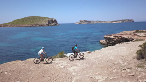 antena - dos personas andan en bicicleta al lado del océano en ibiza, españa, plano general